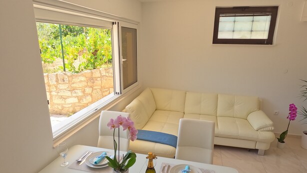 A dining area with a table set for two, a sofa, and a window with a view of greenery.