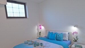 A bedroom with a bed, bedside tables, a window, and a nightstand with a plant.