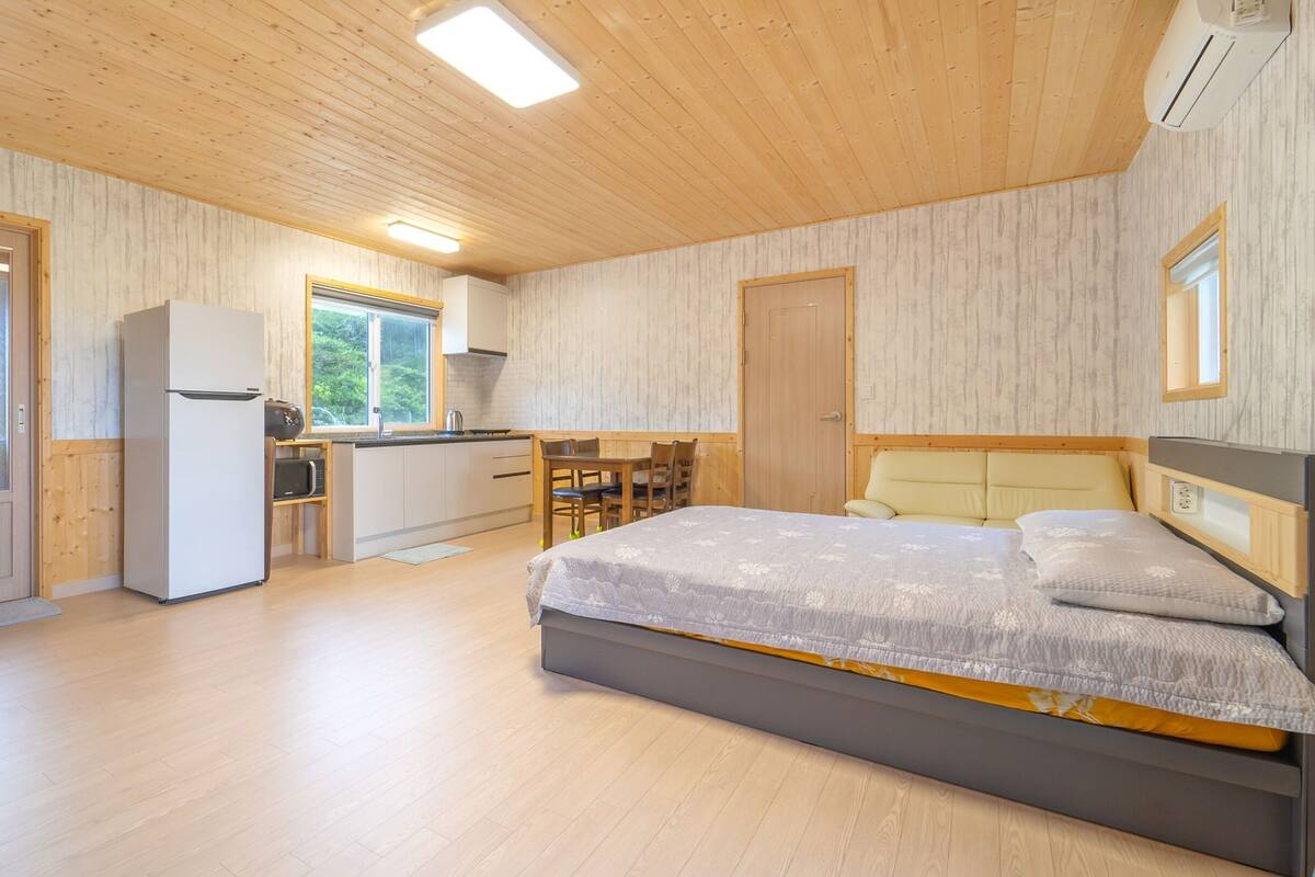 A compact room with a bed, a kitchenette, and a door leading to an outdoor area.