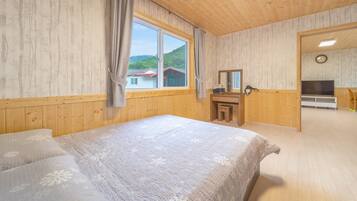 Un dormitorio con una cama grande, un aparador de madera, un espejo, un televisor y una ventana con vistas a casas y árboles.