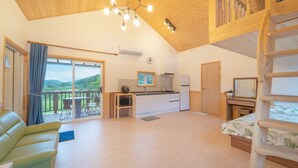 Une pièce confortable avec un plafond en bois, une kitchenette, un balcon avec une table et des chaises, et un lit doté d’une tête de lit en bois.