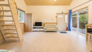 Un vaste espace de vie doté d’un plancher en bois, d’un canapé, d’un téléviseur et d’une porte-fenêtre coulissante donnant sur une terrasse extérieure.