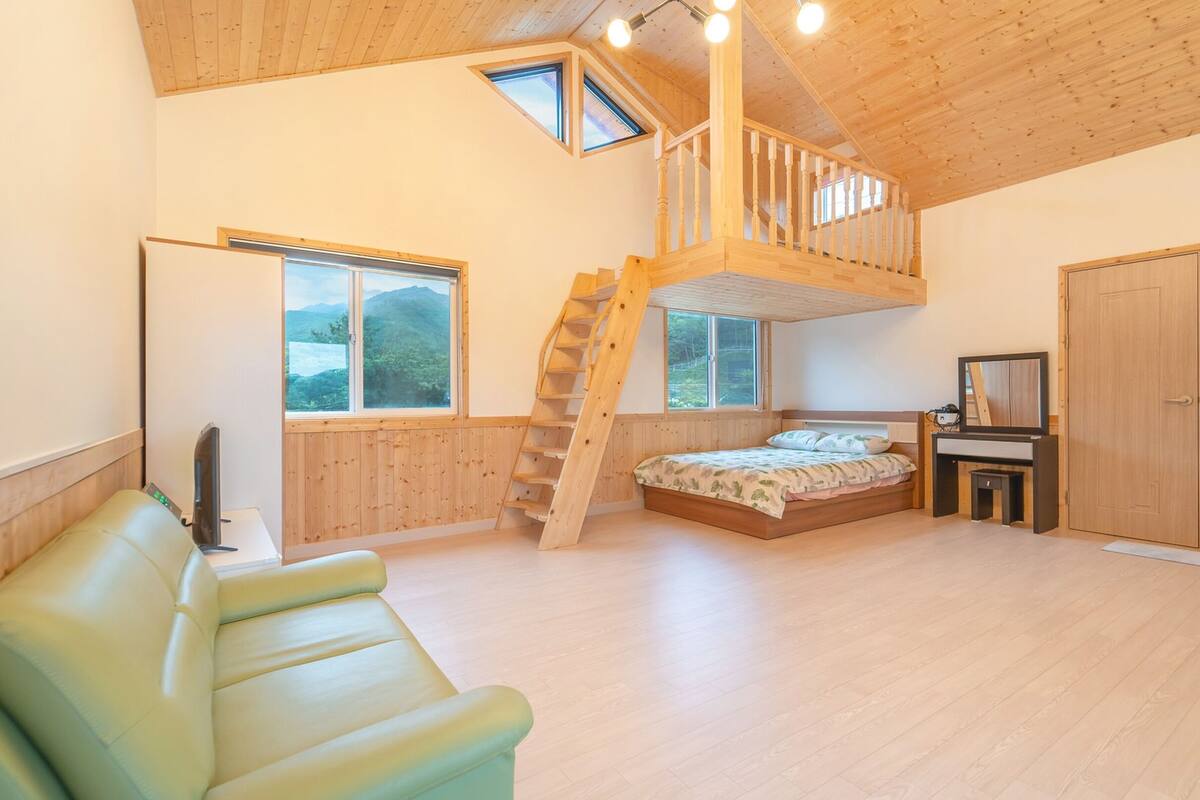 A bedroom with a loft bed, a wooden staircase, a desk, and a television.