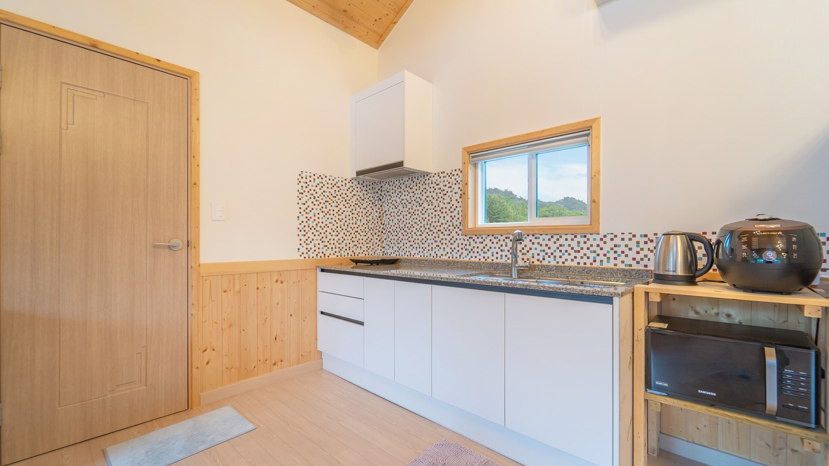 A modern kitchen with white cabinets, a patterned backsplash, a window with a view, and a Samsung microwave.