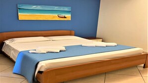 Una cama bien tendida con una colcha azul y ropa de cama blanca, un cabecero de madera y un cuadro de una playa en la pared.