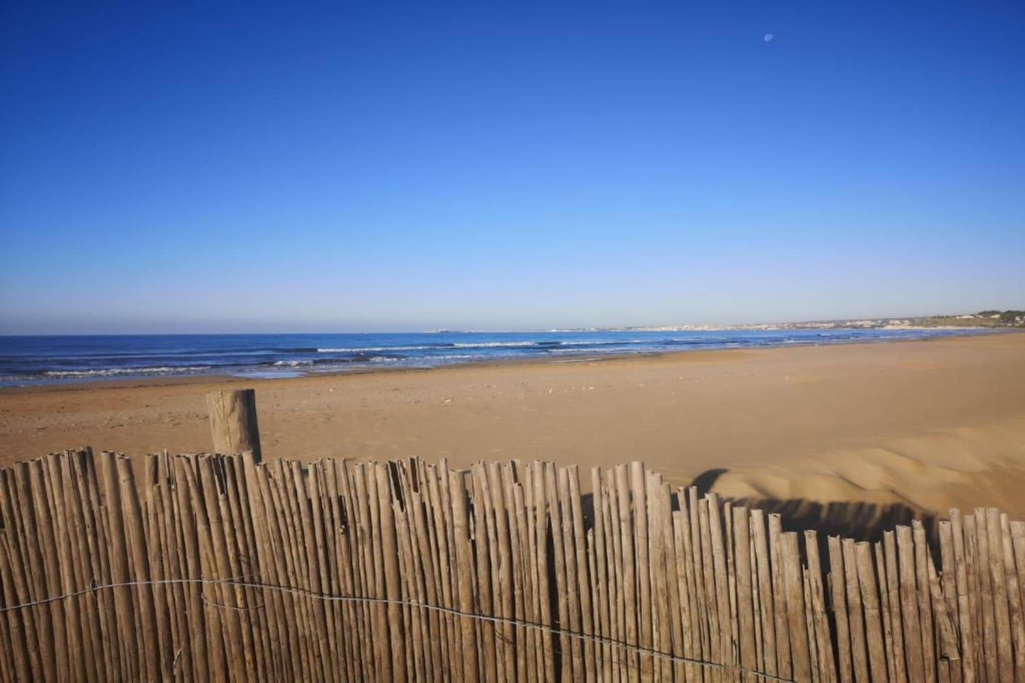Una playa con una valla de madera en primer plano y un cielo azul despejado.