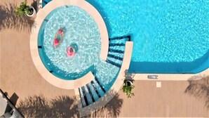 Una bañera de hidromasaje circular con dos personas adentro, rodeada por una piscina.