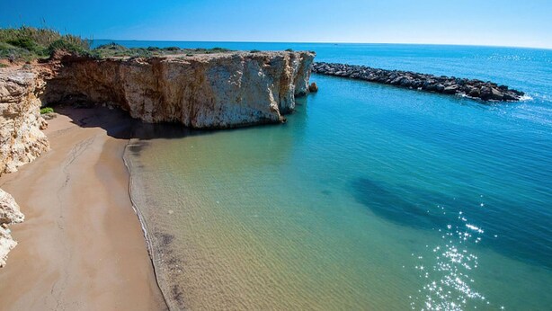 Un paisaje costero con una playa arenosa, acantilados rocosos y aguas azules tranquilas.