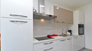 A modern kitchen with white cabinetry, a stainless steel range hood, a sink with a red cleaning tool, and a built-in oven. - House 2177/55666 (Istria - Pula), 2500m from the beach (Pula)