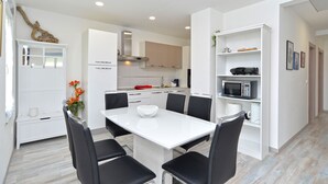 A modern kitchen with white cabinetry, a dining table with four chairs, and a microwave on a shelf. - House 2177/55666 (Istria - Pula), 2500m from the beach (Pula)