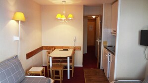 Habitación compacta con sofá, una pequeña mesa, kitchenette y televisor montado en la pared.