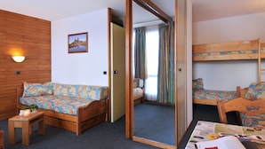 A room with a wooden floor, a sofa, a small table with a candle, a bunk bed, and a mirror.