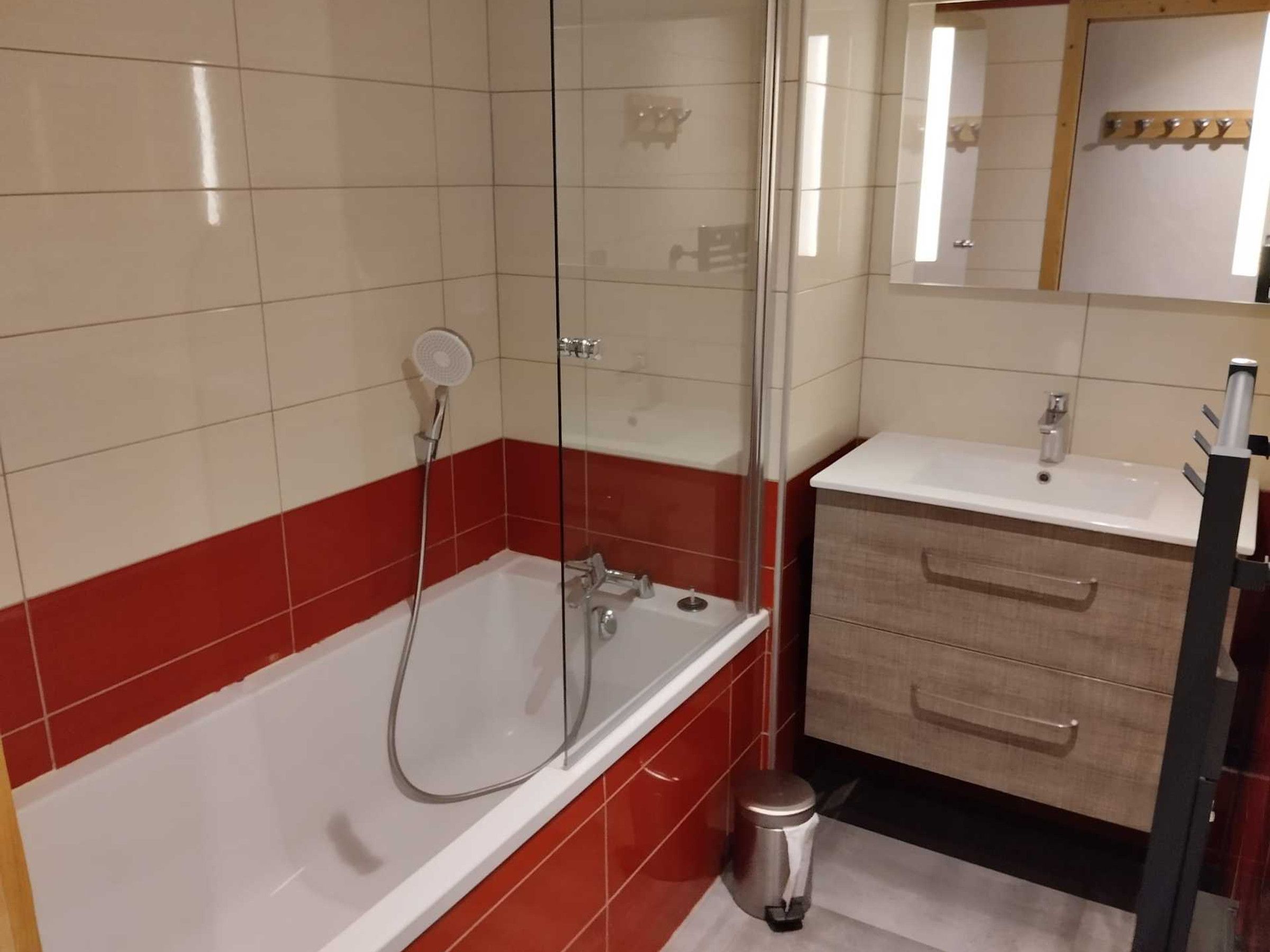 Un bagno con doccia vetrata, lavandino bianco e mobile contenitore in legno.