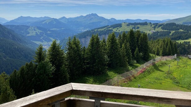 Eine gebirgige Landschaft mit einem Holzzaun und Blick auf ferne Berge.