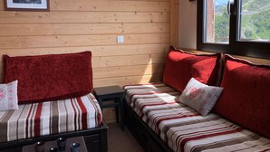 Ein gemütliches Zimmer mit Holzwänden, zwei Betten mit gestreifter Bettwäsche, roten Kissen und einem gerahmten Bild an der Wand.