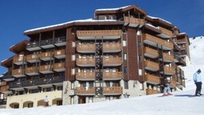 Un hôtel à plusieurs étages doté de balcons, de pistes de ski et surplombant un ciel d’un bleu éclatant.