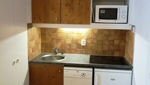 Une cuisine de taille réduite, dotée de meubles en bois, d’un four à micro-ondes, d’un évier et d’un lave-vaisselle.