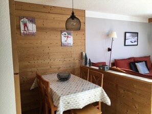 A dining area with a wooden wall, a table with a patterned tablecloth, and a hanging light fixture. - Cozy ski-in/ski-out apt, pets allowed (Belle Plagne)