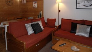 Une pièce chaleureuse avec un mur en bois, un canapé rouge, une table basse en bois et une lampe.