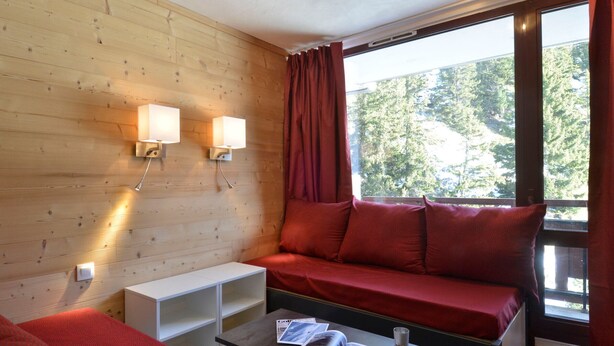 A cozy room with a wooden wall, a red sofa, a small table with a magazine, and two wall-mounted lamps.