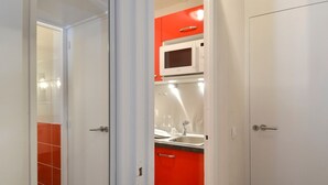 A modern kitchen with white cabinets and a red accent wall, featuring a microwave and a sink.