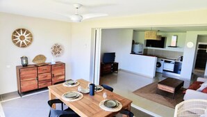A spacious living area with a dining table set for four, a kitchen with modern appliances, and a sliding glass door leading to a balcony. - Sunset on lagoon from the terrace (Marigot)
