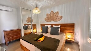 A bedroom with a large bed, a wooden nightstand, a mirror, and a wall-mounted leaf decoration. - Sunset on lagoon from the terrace (Marigot)