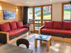 A modern room with two red sofas, a wooden table, and a painting on the wall.