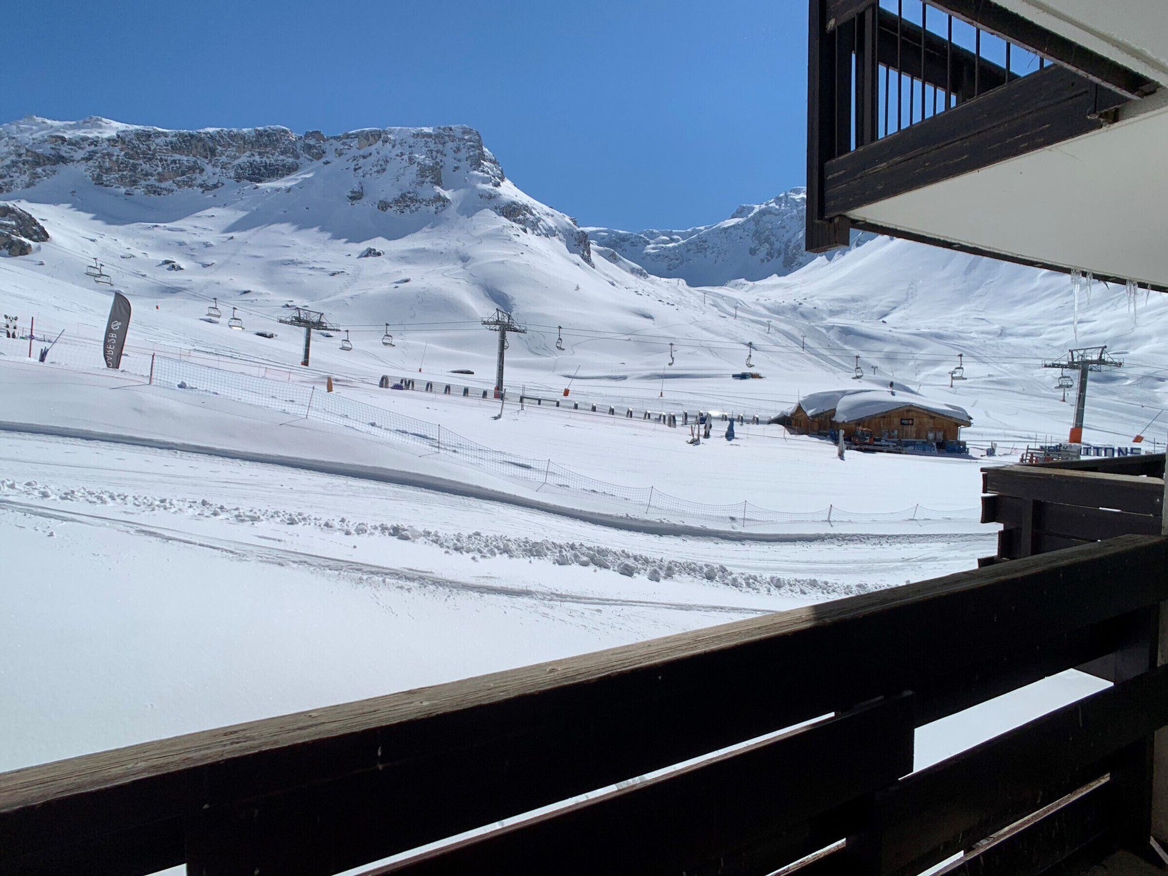 Une piste de ski enneigée, avec des remontées mécaniques, un bâtiment en bois et un ciel bleu dégagé.