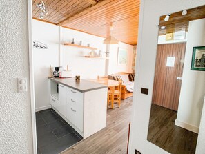 Una cucina compatta con isola centrale, soffitto in legno e zona pranzo con tavolo e sedie in legno.