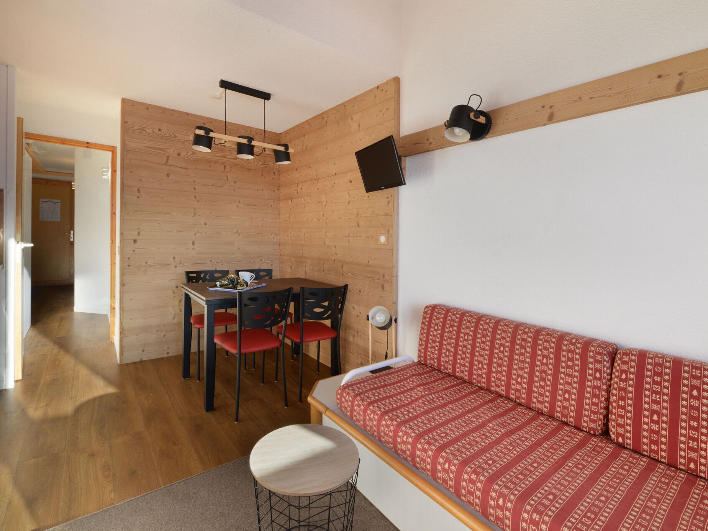 Une pièce chaleureuse avec un mur en bois, un canapé agrémenté de coussins à motifs, une table à manger avec des chaises et un téléviseur fixé au mur.