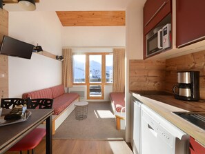 A compact kitchen with a wooden ceiling, a built-in microwave, a coffee maker, and a window with a view of mountains. - Renovated Apt 5 pers ski-in/ski-out (Belle Plagne)