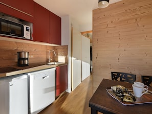 A compact kitchen with a microwave, coffee maker, and dishwasher. There is a dining area with a table and chairs, and a tray with food and cups. - Renovated Apt 5 pers ski-in/ski-out (Belle Plagne)