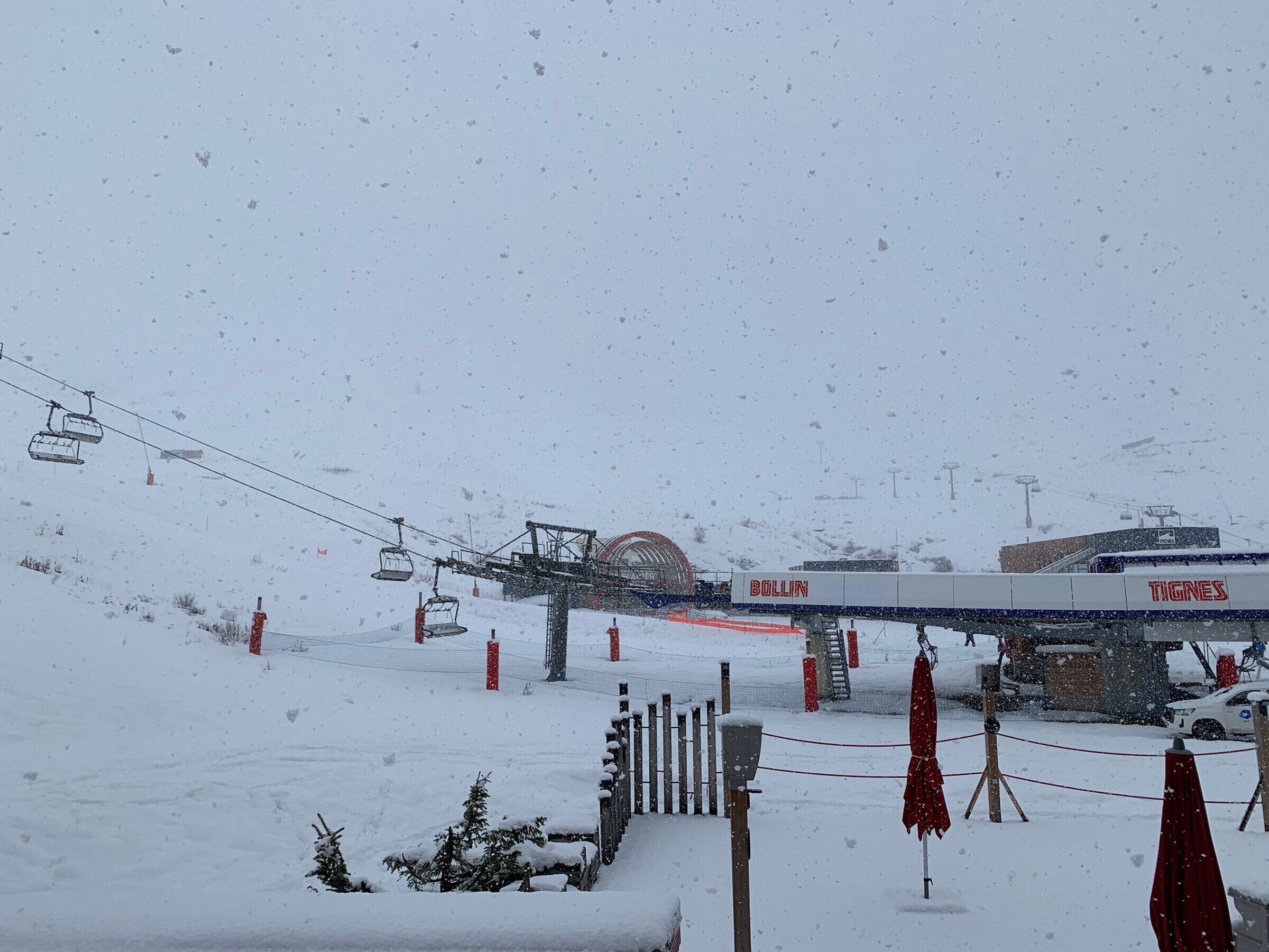 A snow-covered outdoor area with a ski lift, a Bollin and Tignes branded building, and a fenced area with red poles.