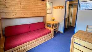 A wooden cabin interior with a red sofa, a small wooden table with a lamp, and a framed picture on the wall.