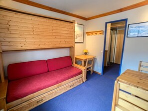 Interior de uma cabana de madeira, com um sofá vermelho, uma pequena mesa de madeira com um abajur e um quadro na parede.