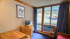 A room with a wooden table, a TV on a small stand, and a window with a view of a water ride.