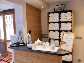 A reception area with a wooden counter, a Buddha statue, a coffee pot, and a sign for Saro Massages. - Renovated apartment near slopes, free parking, pets welcome (La Plagne Montchavin Les Coches)