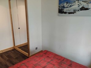 A room with a wooden floor, a red carpet, a white wall, and a painting of a snowy mountain landscape. - Renovated apartment near slopes, free parking, pets welcome (La Plagne Montchavin Les Coches)