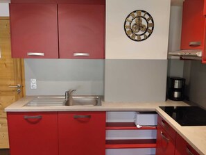 Eine Küche mit roten Schränken, einer Spüle aus Edelstahl, einer Kaffeemaschine und einer Uhr an der Wand.