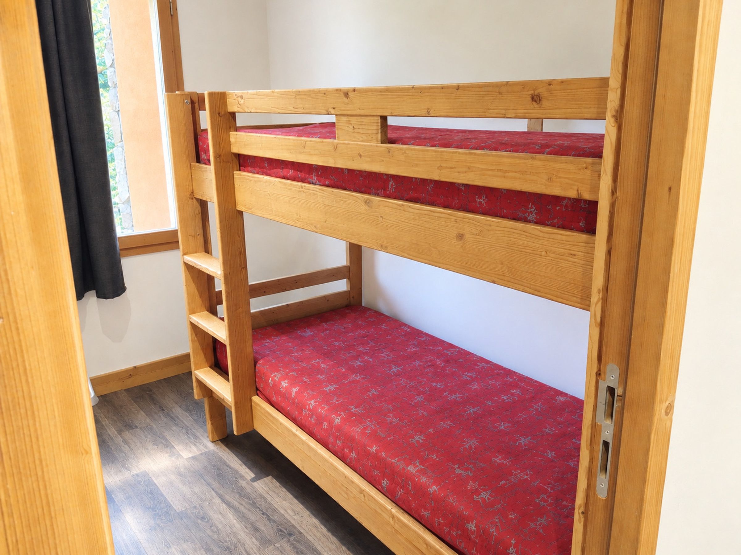 A bunk bed with a red mattress and wooden frame.