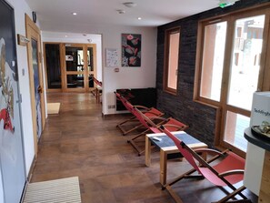 Ein langer Korridor mit Holzboden, einer Sitzecke mit roten Stühlen, einer an der Wand hängenden Karte und einem Fenster mit Blick auf Gebäude.