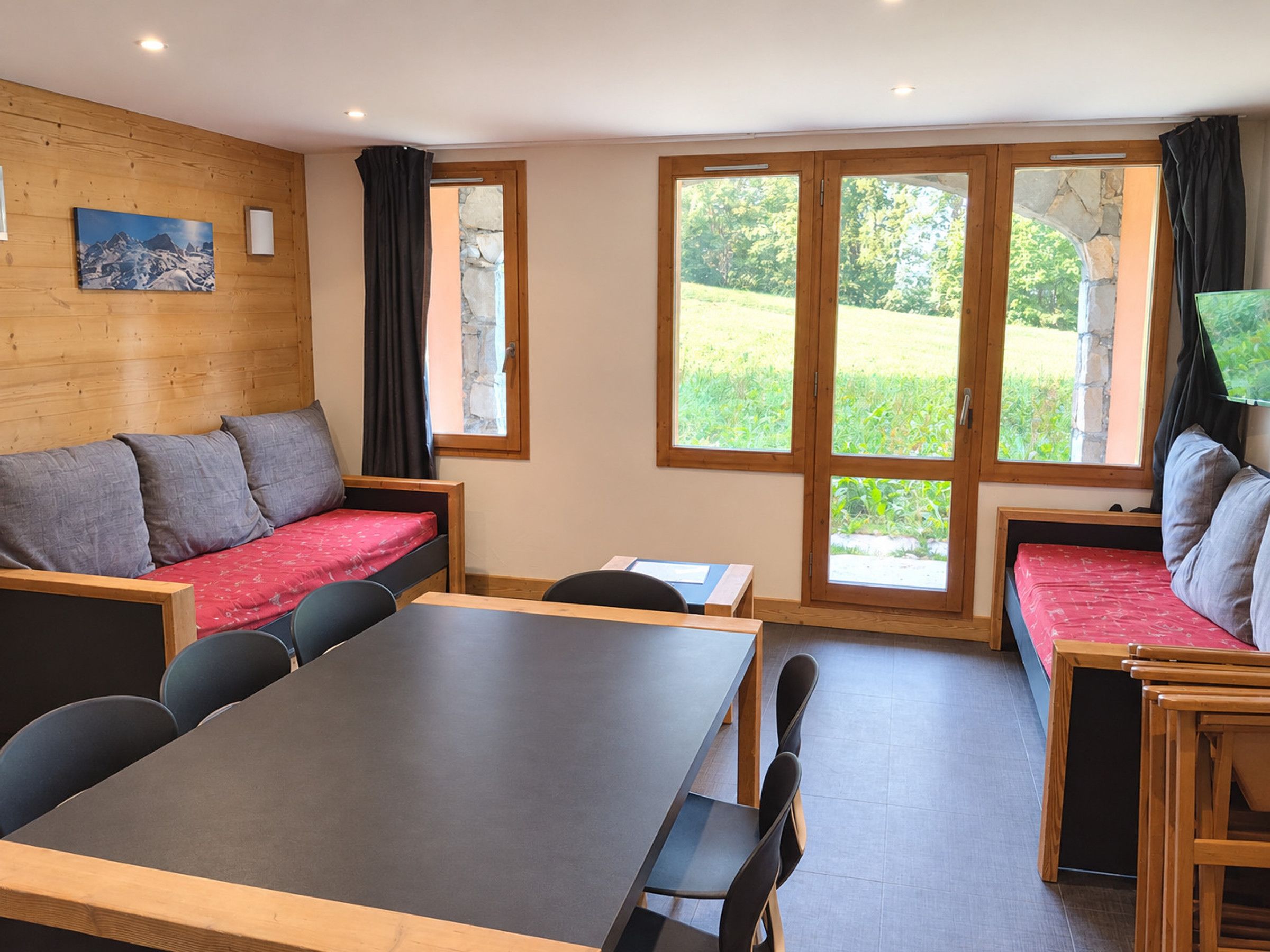 Ein Zimmer mit Holzwand, einer Couch, einem Tisch und einem Fenster mit Blick auf Grünflächen.