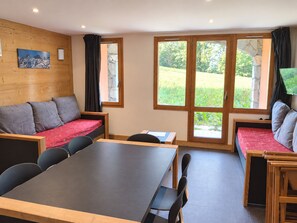 Ein Zimmer mit Holzwand, einer Couch, einem Tisch und einem Fenster mit Blick auf Grünflächen.