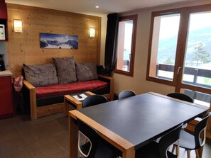 A cozy room with a wooden wall, a red sofa, a dining table, and chairs. - Renovated ski-in apartment with free parking, pets allowed (La Plagne Montchavin Les Coches)