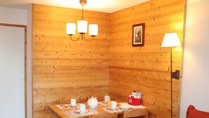 Una habitación con paneles de madera y una mesa preparada para el desayuno, con tazas, una tetera y un bolso rojo.