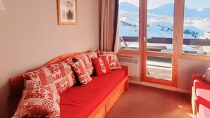 Un cuarto acogedor con un sofá rojo, un cuadro enmarcado en la pared y un ventanal con vistas a un paisaje nevado.