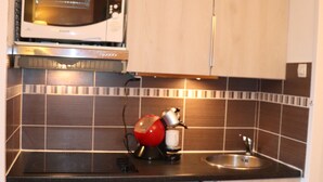Una cocina con microondas, hervidor rojo, lavavajillas y salpicadero de azulejos.