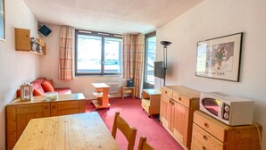 A compact living space with a wooden dining table, a sofa, a small TV, and a microwave.