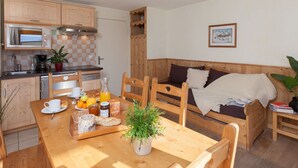 A compact kitchen with wooden cabinets, a dining table with breakfast items, and a cozy seating area with a sofa and cushions. - Ski-in studio with WiFi and pets allowed (Briançon)